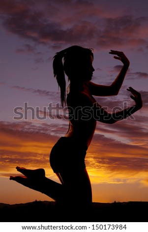 A woman silhouetted in the sunset hands and feet up.
