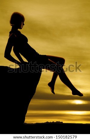 A silhouette of a woman reaching out her toe on a ledge with a beautiful sunrise.