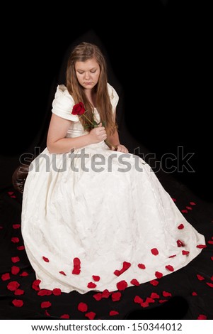 A young woman in a white formal dress is sitting with a rose.