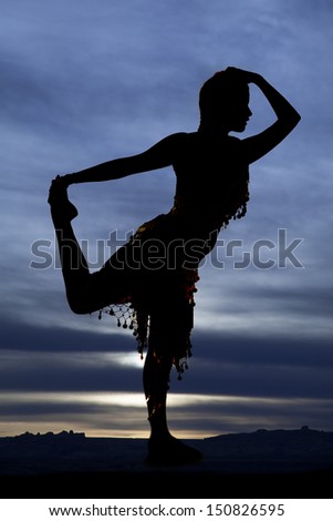A silhouette of a woman dancing and holding her foot with a blue sunset in the background