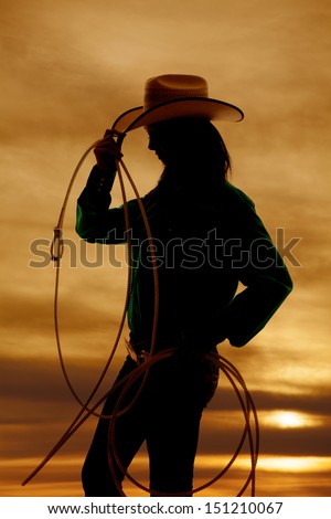 A silhouette of a woman with a rope and cowgirl hat, with a beautiful sunset in the background.