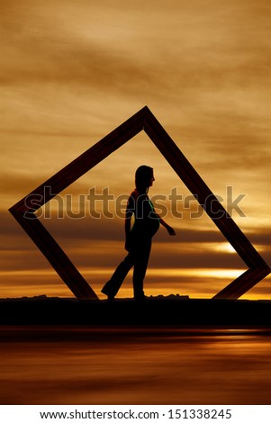 A pregnant woman walking framed in a picture frame.