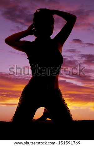 A silhouette of a woman on her knees with her hands by her hair.
