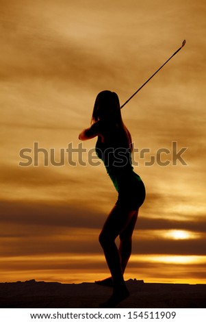 A silhouette of a woman swinging her golf cub in the outdoors.