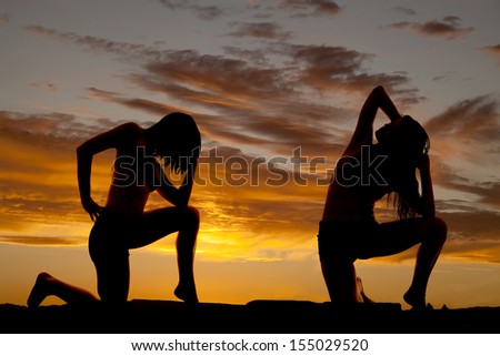 A silhouette of a woman kneeling and posing and stretching in the outdoors.