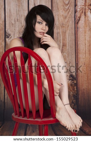 A woman sitting in a red chair with her legs brought up to her chest.