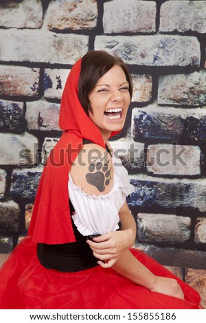 A woman laughing in her red hood and a wolf tattoo on her arm.