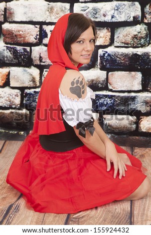 A woman with a serious expression on her face in her red hood showing off her wolf paw print on her shoulder.
