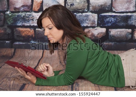 A woman laying down and working on her tablet with a serious expression