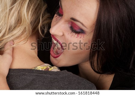 A female vampire getting ready to take a bite out of a woman\'s neck.