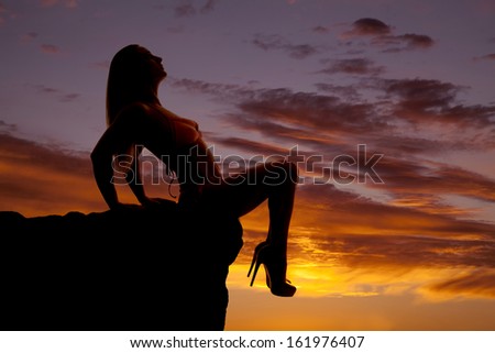 A woman in the sunset in a bikini sitting legs over edge.