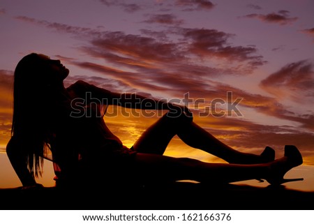 A silhouette of a woman sitting and leaning back while looking up.