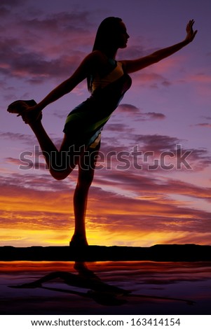 a silhouette of a woman holding on to her foot with her arm out.