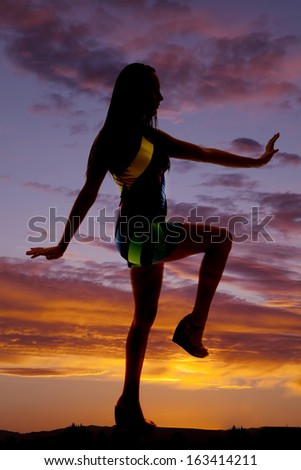 a silhouette of a woman  her foot out in front with her arm out.