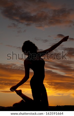 A silhouette of a woman kneeling down reaching up.