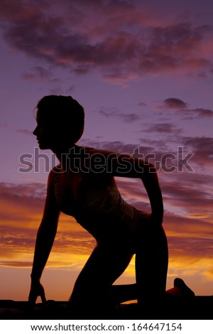 A silhouette of a woman kneeling in the outdoors.