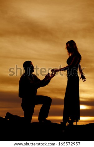 a silhouette of a man on his knee to propose to his woman .