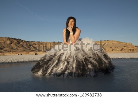 a woman in her formal dress on a frozen lake with mountains in the background.