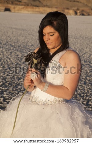 a woman in her formal dress in the outdoors on a frozen lake looking down at her flower.