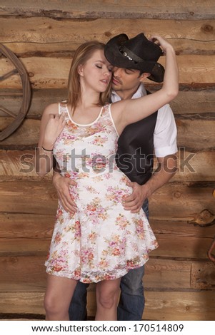 A western couple is standing together and she is holding his hat.