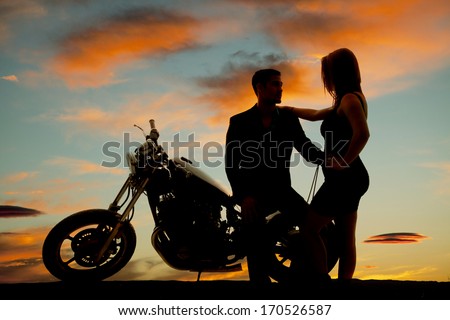 A silhouette of a man sitting on his bike holding on to his woman.
