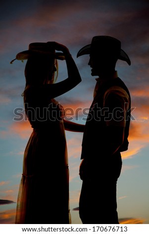 A silhouette of a woman in her cowgirl hat looking at her cowboy.