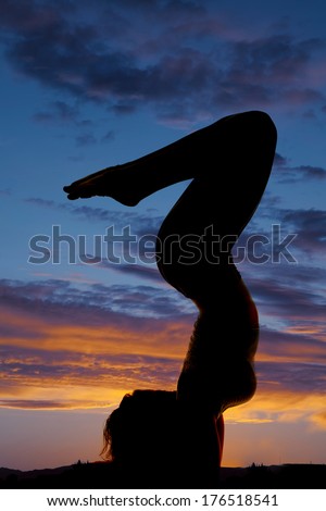 A woman is silhouetted in the sunset on her arms with her legs up.