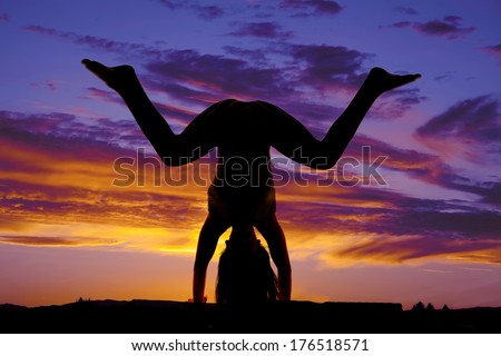 A woman in the sunset silhouette doing a hand stand with knees bent.