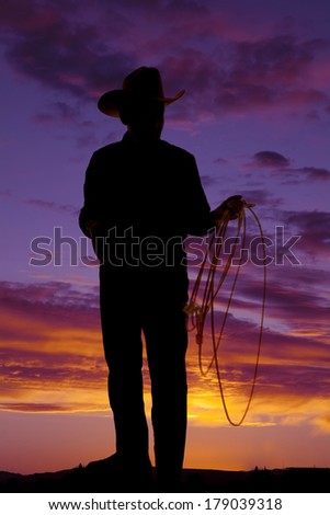A silhouette of a older cowboy holding on to his rope.