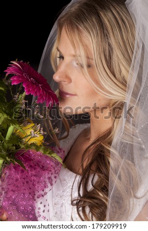 A woman in a wedding dress smelling some flowers.