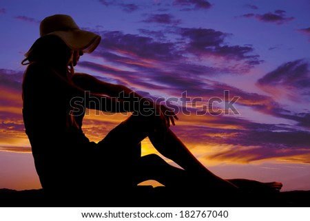 A silhouette of a woman in the outdoors in her sundress and floppy hat.