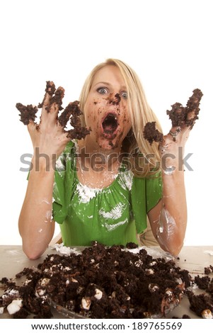 A woman with cake and frosting all over her face and hands with a shocked expression.