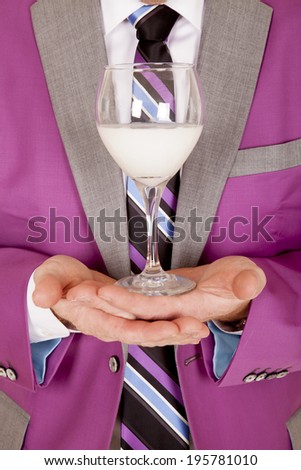 A close up picture of a man holding a glass in his hands in front of his chest.