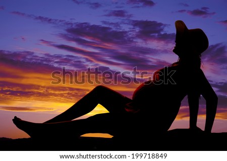 A silhouette of a woman sitting back on a bench in the outdoors.
