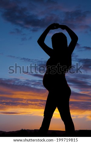 A pregnant woman standing in the outdoors with her arms up in the air.