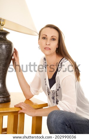 a woman kneeling down by a lamp with a serious expression on her face.