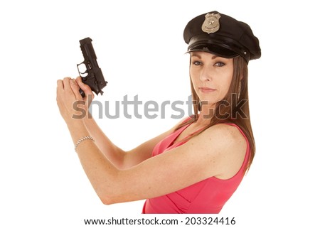 A woman in her pink dress looking to the camera holding on to a gun wearing her cop hat.