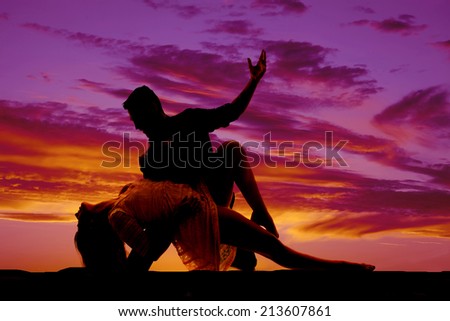 A silhouette of a woman and man doing a dance move in the outdoors.