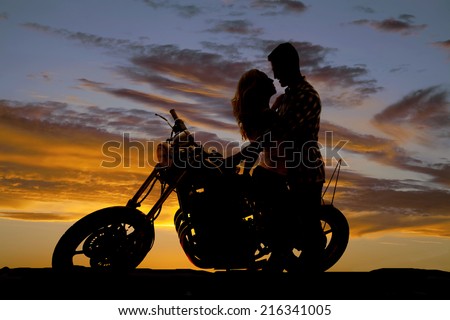A man looking down at his woman, as she sits on a motorbike, looking into her eyes.