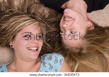 Two girl teenagers laying on the floor looking and laughing at each other.