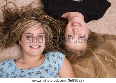 Two teenage girls laying together with their heads together smiling.