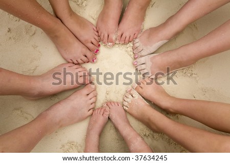 A bunch of kids feet laying in a circle in the sand.