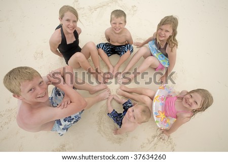 Six children sitting in a circle in with their feet together in the sand.
