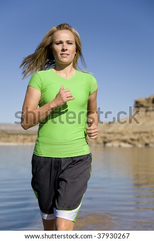 A woman running in the lake water with a beautiful back drop of rocks and mountains.