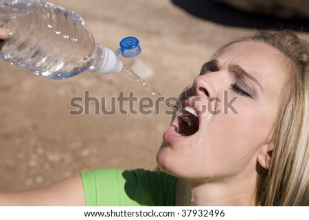 A woman squirting water from a water bottle into her mouth.