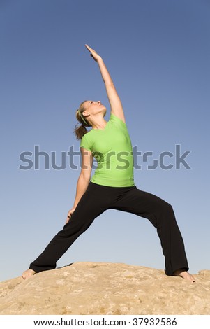 A woman doing yoga warrior three while standing on a rock in the outdoors.