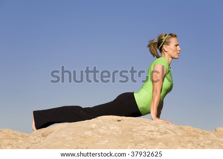 A woman doing the yoga position upward dog on a rock in the outdoors.