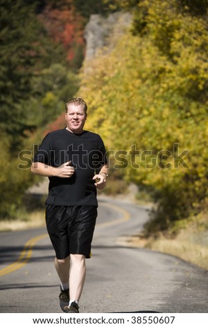 A man running down a road with the fall color of trees behind him.