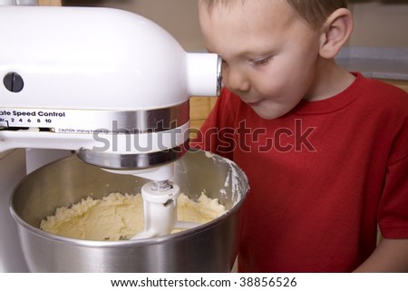 A boy peeking and watching the mixer mix the dough.