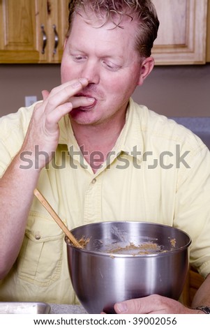 A man enjoying and licking his fingers after eating cookie dough.